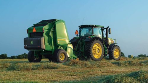 A John Deere tractor uses a baler to collect and bale hay on farm land.