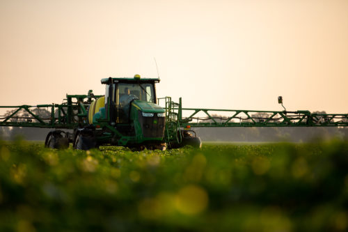 John Deere tractor driving with irrigation arms through a green crop field.