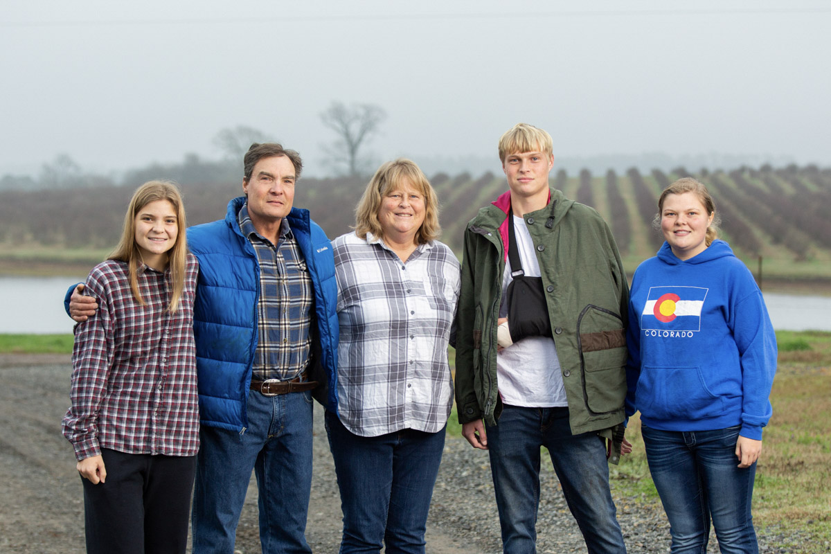 Farm family of five standing together with agricultural fields in background